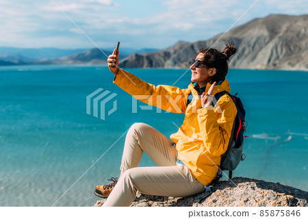 A traveler takes a selfie on her phone against the background of the sea, Close-up. A traveler on the seashore. A girl holds a phone in her hands against the background of a beautiful sea. 85875846