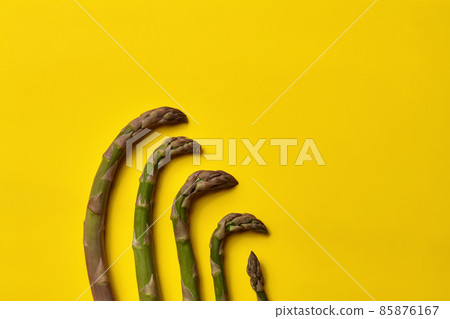 Five green ripe asparagus stems laid out from large to small size on yellow background. Healthy nutrition, seasonal vegetables. Close up, copy space Five green ripe asparagus stems laid out from large to small size on yellow background. Healthy nutrition, seasonal vegetables. Close up, copy space 85876167