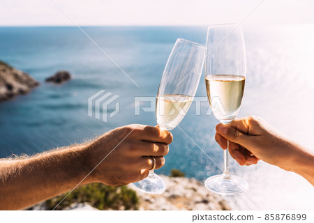 Hands holding champagne glasses over the sea. Romantic vacation. Two hands holding champagne glasses on the background of the sea. Toast with champagne glasses on the seashore. Copy space Hands holding champagne glasses over the sea. Romantic vacation. Two hands holding champagne glasses on the background of the sea. Toast with champagne glasses on the seashore. Copy space 85876899