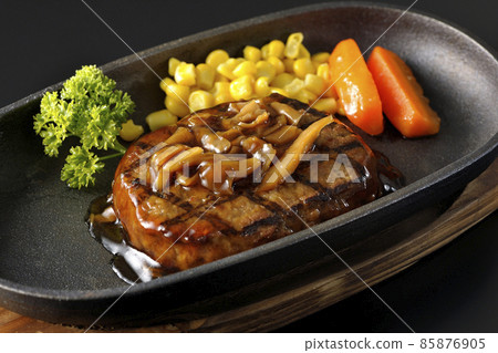 Japanese-style hamburger steak with parsley, carrot glass, corn, and mushroom sauce on an iron plate shot on a black background Japanese-style hamburger steak with parsley, carrot glass, corn, and mushroom sauce on an iron plate shot on a black background 85876905
