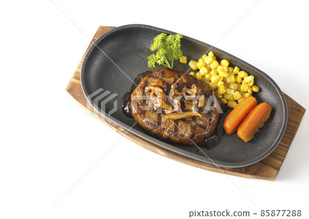 A bird's-eye view of a Japanese-style hamburger steak with parsley, carrot glass, corn, and mushroom sauce on an iron plate on a white background. 85877288