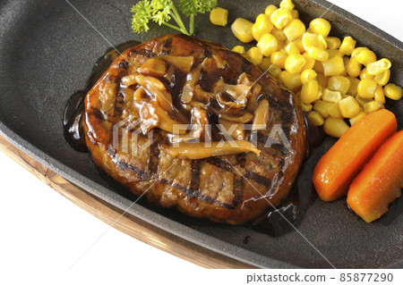 A bird's-eye view of a Japanese-style hamburger steak with parsley, carrot glass, corn, and mushroom sauce on an iron plate on a white background. 85877290