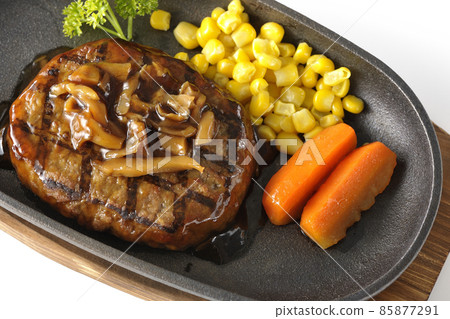 A bird's-eye view of a Japanese-style hamburger steak with parsley, carrot glass, corn, and mushroom sauce on an iron plate on a white background. 85877291