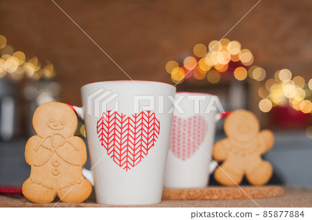 Two cups and gingerbread men on table with garlands blurred background. Kitchen is decorated for New Year. Interior details with Christmas decor.. 85877884