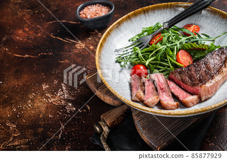 Grilled Top sirloin beef meat steak in plate with vegetable salad. Dark background. Top view. Copy space 85877929