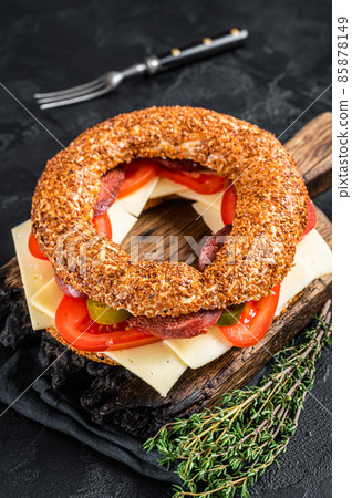 Simit bagel sandwich with lettuce, tomato, yellow cheese and ham. Black background. Top view 85878149