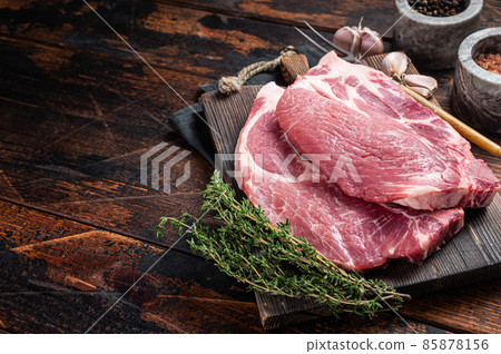 Butcher raw Pork steak from raw neck fillet meat on wooden board with herbs. Wooden background. Top view. Copy space 85878156