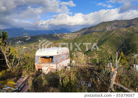 Old abandoned rusted roulotte Rv van in green field 85879087
