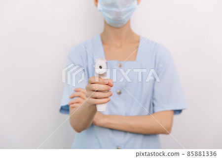 Temperature measurement gun in doctor hands. Close-up shot of doctor wearing protective surgical mask ready to use infrared isometric thermometer gun to check body temperature for virus symptoms. Temperature measurement gun in doctor hands. Close-up shot of doctor wearing protective surgical mask ready to use infrared isometric thermometer gun to check body temperature for virus symptoms. 85881336
