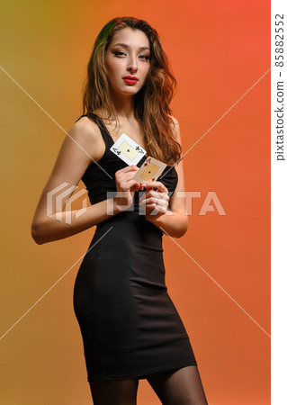 Brunette model with earring in nose, in black dress. Showing two aces while posing on colorful background. Gambling, poker, casino. Close-up 85882552