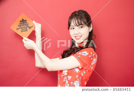 身穿傳統旗袍旗袍的亞洲年輕女子紅色背景上手持寫著中字“春”(意思為美好、幸福)春聯慶祝新年。 身穿傳統旗袍旗袍的亞洲年輕女子紅色背景上手持寫著中字“春”(意思為美好、幸福)春聯慶祝新年。 85883451