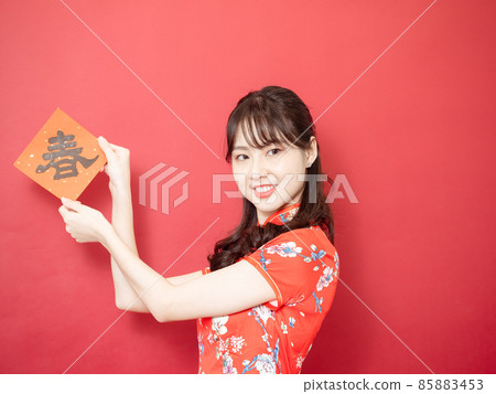 身穿傳統旗袍旗袍的亞洲年輕女子紅色背景上手持寫著中字“春”（意思為美好、幸福）春聯慶祝新年。 85883453