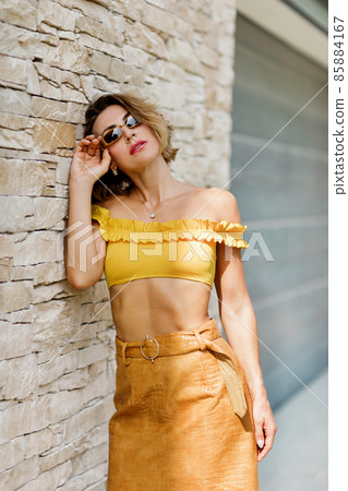 Portrait of a young woman in sunglasses posing near the wall 85884167