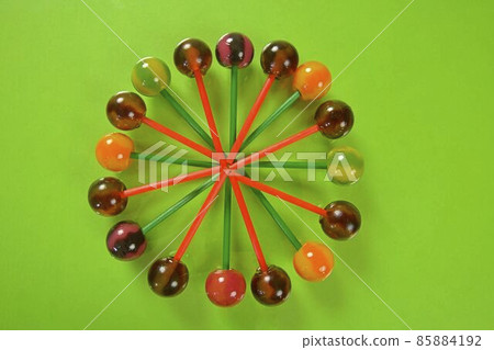 Various colorful lollipops on pastel background. Bright juicy colored lollipops on a green background. Lollipops in the form of a flower. Fruit candy 85884192