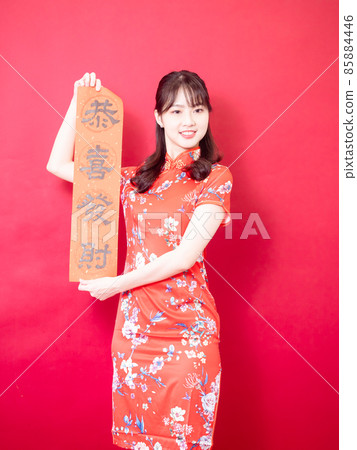 Young Asian woman wearing traditional cheongsam cheongsam celebrating new year holding spring couplet with Chinese text "Gong Xi Fa Cai" on red background. Young Asian woman wearing traditional cheongsam cheongsam celebrating new year holding spring couplet with Chinese text "Gong Xi Fa Cai" on red background. 85884446