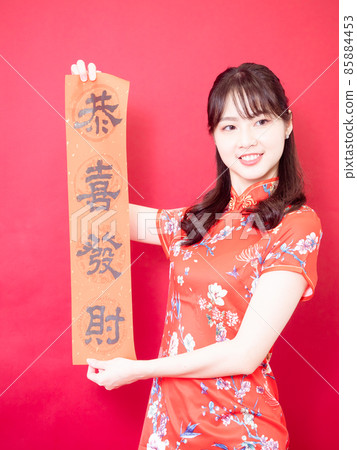 身穿傳統旗袍旗袍的亞洲年輕女子紅色背景上手持寫著中文字“恭喜發財”春聯慶祝新年。 身穿傳統旗袍旗袍的亞洲年輕女子紅色背景上手持寫著中文字“恭喜發財”春聯慶祝新年。 85884453