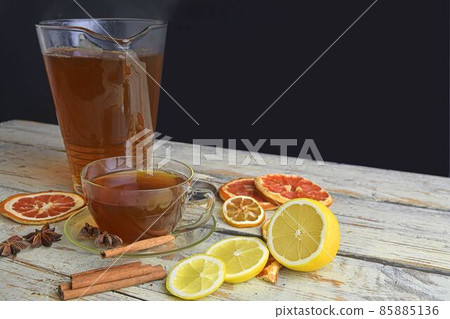 Glass cup of black tea with cinnamon sticks, anise star, lemon and dried fruit on white wooden table background. Jug of black tea. Large copy space Glass cup of black tea with cinnamon sticks, anise star, lemon and dried fruit on white wooden table background. Jug of black tea. Large copy space 85885136