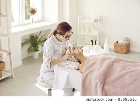 Beautician, cosmetologist or dermatologist cleaning skin on woman's face after chemical peel. Specialist at spa salon wiping young lady's face with wet towel after doing professional facial treatment 85885616