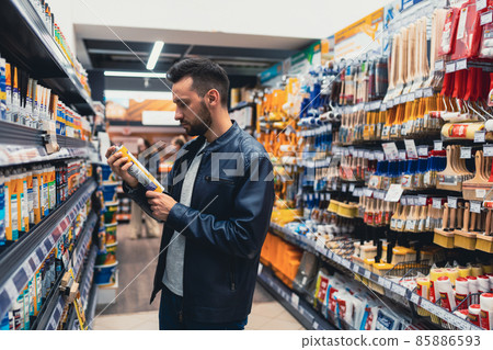 a man in a hardware store chooses adhesive sealant next to a rack of building materials 85886593