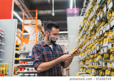 a man chooses a product in a building materials store next to a showcase with self-tapping screws a man chooses a product in a building materials store next to a showcase with self-tapping screws 85886594