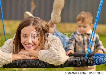 Young woman lying on swing and standing child 85887038