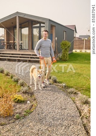 Man with dog on leash walking near country house Man with dog on leash walking near country house 85887041