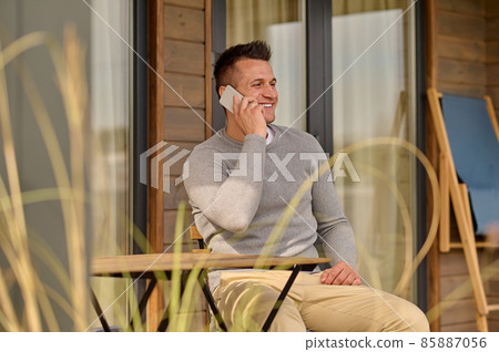 Man talking on smartphone sitting outdoors 85887056