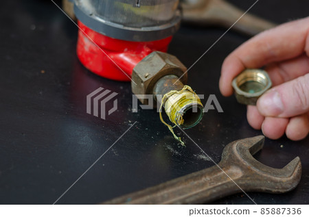 Man's hand is holding a brass plug in front of the water meter and wrenches.  85887336