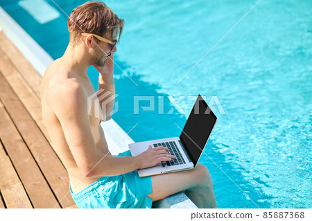 Young man at the swimming pool working on a laptop 85887368