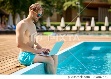 Young man at the swimming pool working on a laptop 85887369