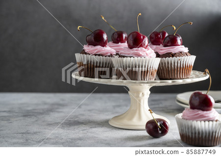 Chocolate cupcakes with fresh cherries and pink cream on cake stand. Beautiful dessert. Dark background. Chocolate cupcakes with fresh cherries and pink cream on cake stand. Beautiful dessert. Dark background. 85887749