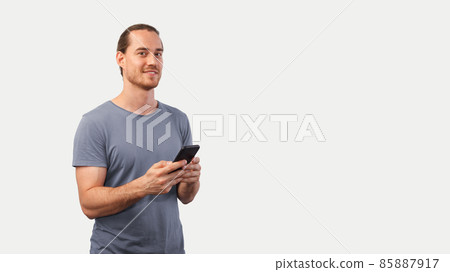 Blonde unshaven man holds a smartphone in his hands and looks into the camera smiling. A proud smiling man uses a mobile phone 85887917