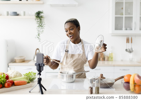 Satisfied millennial black lady with open mouth in apron prepares dinner, shows her dish, shoots video for food blog 85888380