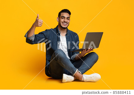 Cheerful arabic guy with laptop showing thumb up Cheerful arabic guy with laptop showing thumb up 85888411