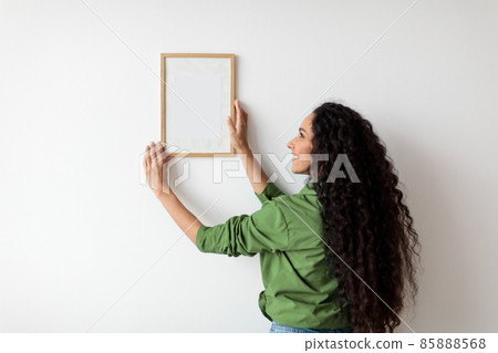 Lady Hanging Picture In Frame On Wall Decorating House Indoors 85888568