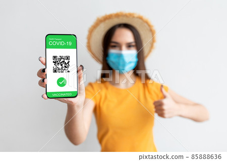 Electronic health passport. Young woman wearing face mask and holding smartphone with digital e-passport in hand 85888636