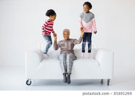 African islamic woman in hijab sitting on couch while daughters jumping 85891269