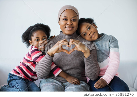 Mother in headscarf showing heart shape while daughters hugging her 85891270