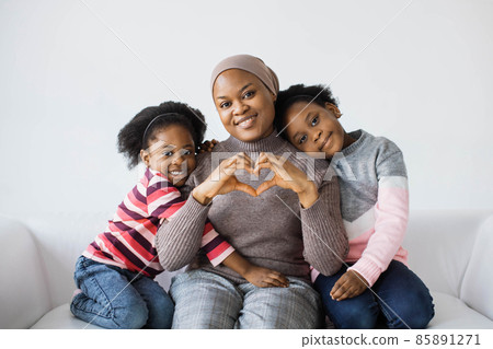 Mother showing heart shape while daughters hugging her Mother showing heart shape while daughters hugging her 85891271
