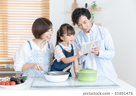 Mom, elementary school girl and dad cooking while looking at the tablet in the kitchen Mom, elementary school girl and dad cooking while looking at the tablet in the kitchen 85891478