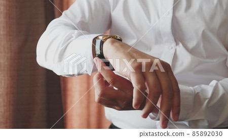 A man looks at the dial of the clock on his hand, to check the time, to be late for work in the morning, the businessman is punctual, the business plan is on time 85892030