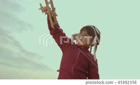 little child in a helmet plays with an airplane against sky, childhood dream to fly, kid wants to become an airplane pilot, imagination, happy family, cheerful baby makes illusion flight in fantasies 85892356
