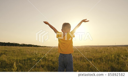 happy child boy prays, spreading his hands to the sides at sunset, kid praying to the sun in sky, pulling helping hand, enjoying freedom outdoors walking in nature in park, inspiring childhood dream happy child boy prays, spreading his hands to the sides at sunset, kid praying to the sun in sky, pulling helping hand, enjoying freedom outdoors walking in nature in park, inspiring childhood dream 85892582