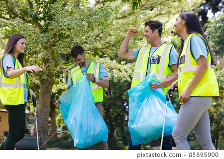 Cheerful male and female volunteers collecting garbage in plastic bags during cleanup in park Cheerful male and female volunteers collecting garbage in plastic bags during cleanup in park 85895900