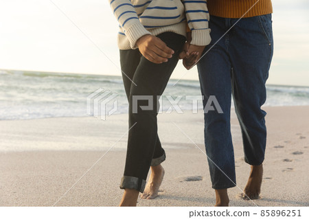 Low section of biracial couple holding hands while walking together on shore at beach during sunset Low section of biracial couple holding hands while walking together on shore at beach during sunset 85896251
