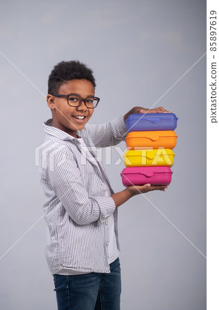 Joyous schoolboy demonstrating his food containers before the camera Joyous schoolboy demonstrating his food containers before the camera 85897619
