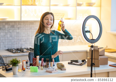 Smiling young woman presenting hairspray during online beauty tutorial 85898112