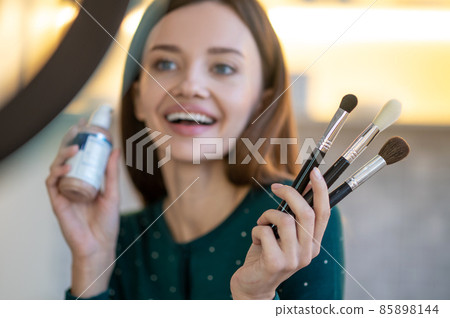 Young woman holding face brushes and smiling Young woman holding face brushes and smiling 85898144