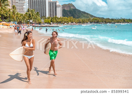 Hawaii surf lifestyle couple of surfers going surfing in Waikiki beach, Honolulu, Oahu island. USA travel. Fun summer tourist vacation destination activity 85899341