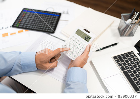 Working Man Conept The male officer sitting at his desk, holding the calculator, and pressing it 85900337